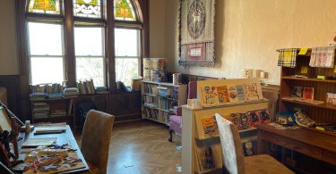 Large stained glass window with desks and book shelves with children's books and curriculums