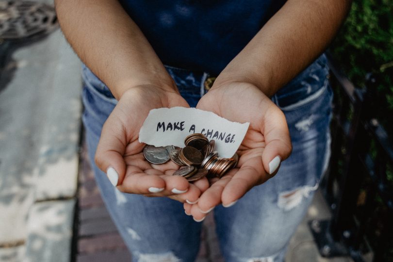 hands holing a slip of paper that reads "Make a Change" with coins