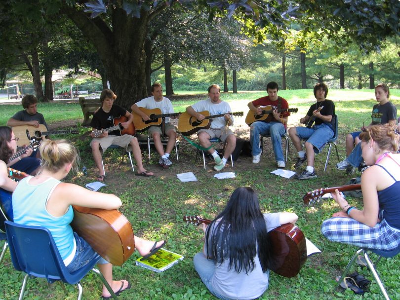 circle of people playing guitar at camp