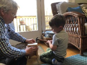 man helping young boy hammer nail into a block of wood