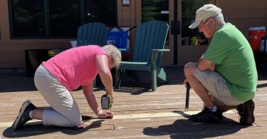 a couple drilling nails into a deck